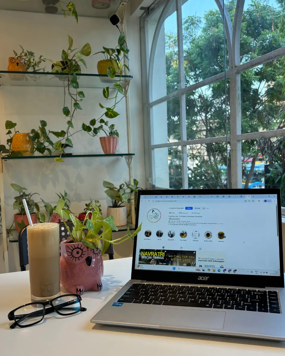 A laptop and a tall iced drink on a café table beside a small potted plant