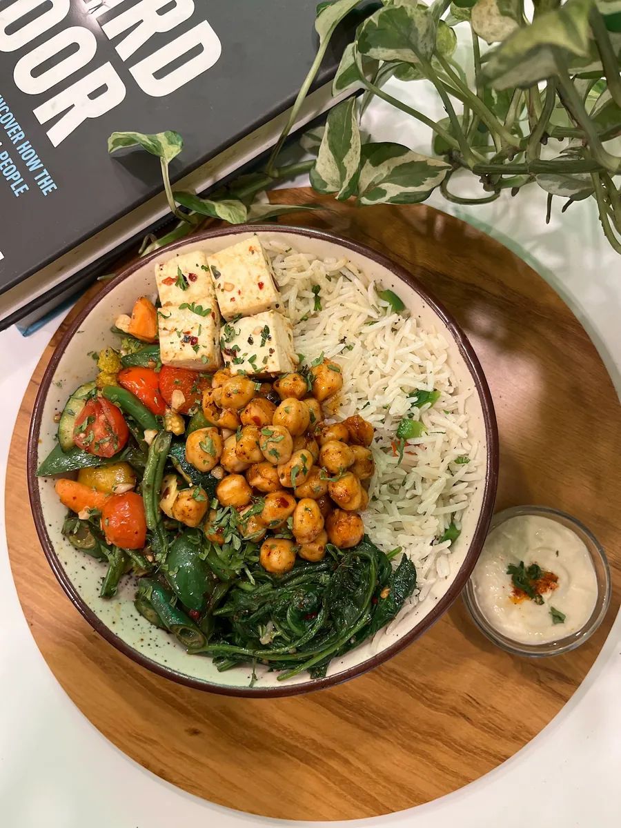 A grain bowl with roasted vegetables, chickpeas and paneer on a wooden board