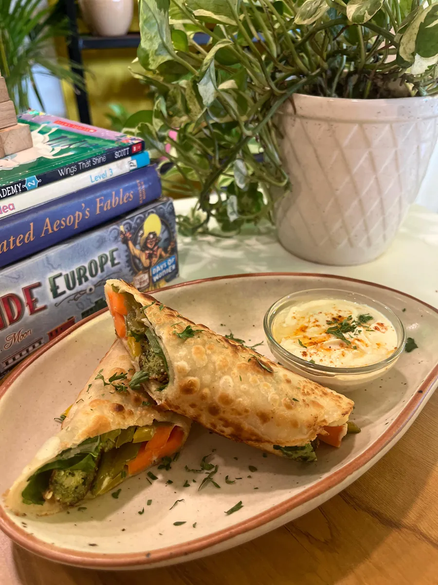 A stuffed paratha roll served with a dip on a speckled ceramic plate beside a stack of books