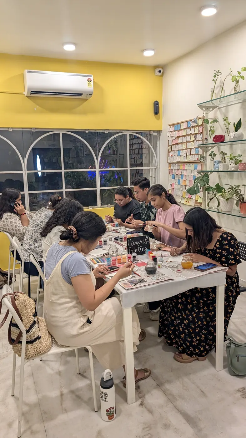 A workshop in progress at a long white table against a yellow wall with arched windows